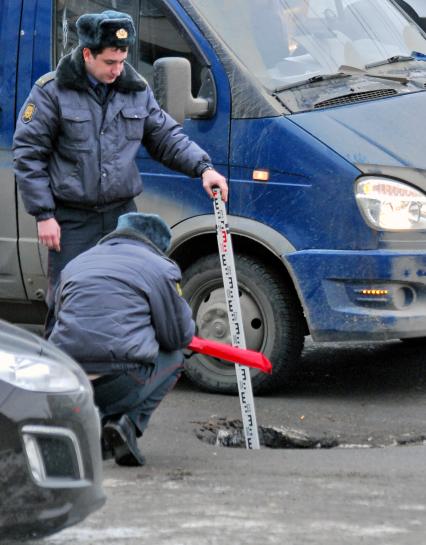 Два сотрудника ГИБДД измеряют метром глубину ямы на проезжей части.