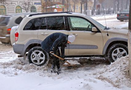 Девушка расчищает снег рядом с автомобилем.