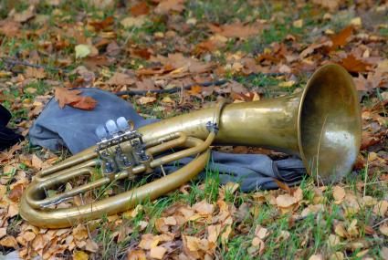 Медный духовой инструмент лежит на траве (туба), среди осенних листьев.