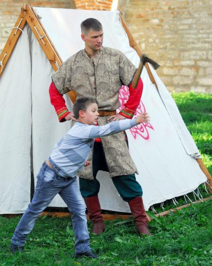 Мальчик метает русский боевой топорик, мужчина в костюме русского воина смотрит за соблюдением техники безопасности.