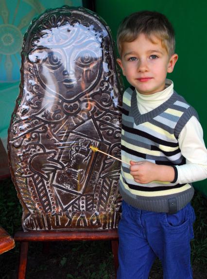 Мальчик стоит рядом с большим тульским пряником в форме матрешки.