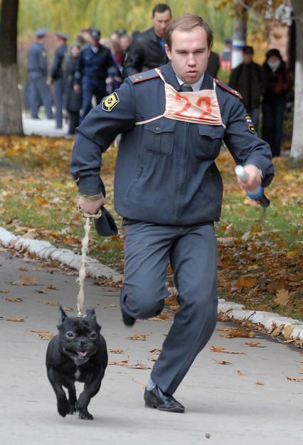 Полицейский на соревнованиях бежит с собакой.