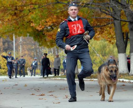 Полицейский на соревнованиях бежит с собакой.