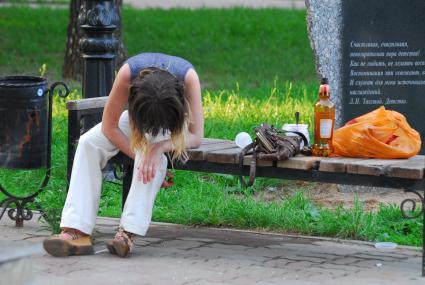 Пьяная девушка сидит на скамейке в парке.