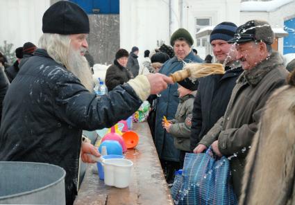 Священнослужитель окропляет прихожан освященной водой.