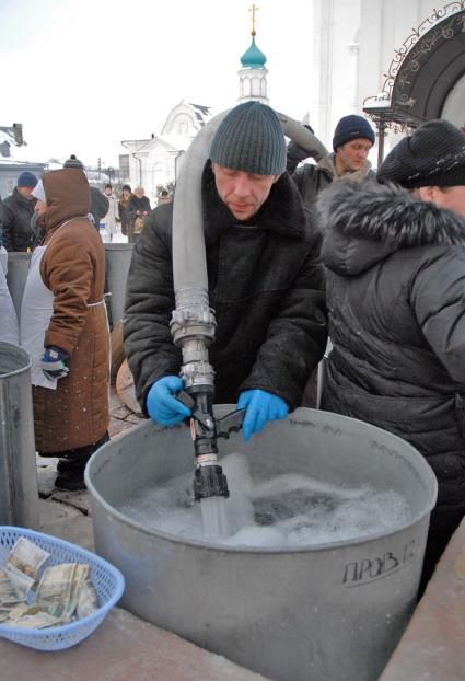 Мужчина наполняет емкость для освященной воды из пожарного рукава.