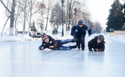 Дети катаются на льду без коньков.