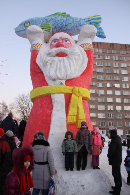 Снежная скульптура Деда Мороза держащего в руках над головой рыбу.