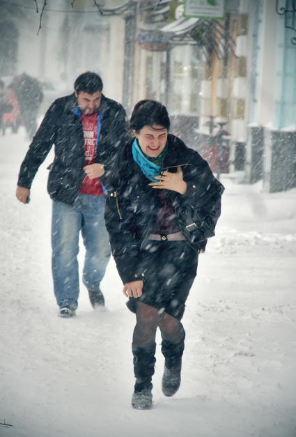 Женщина и мужчина идут по улице в снегопад.