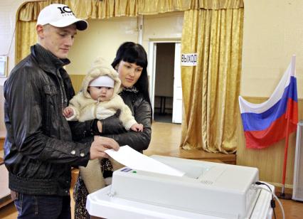 Выборы в муниципалитет Ярославля. На снимке: Молодая семья, мужчина женщина и ребенок опускают бюллетень в электронную урну для голосования.