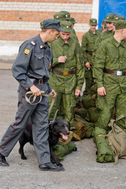 Полицейский кинолог с собакой обследует вещи призывников.