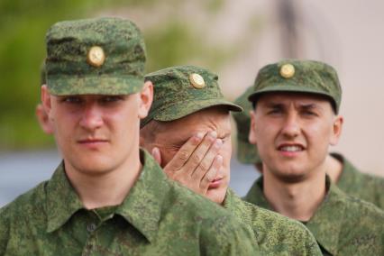 Солдат стоя в строю трет рукой лицо.