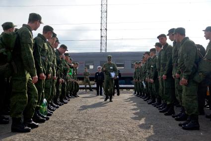 Офицер проходит вдоль строя солдат стоящих перед поездом на вокзале.