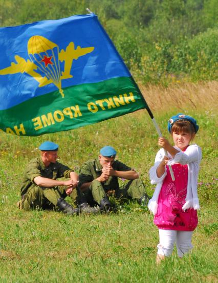 День ВДВ. На снимке: девочка в руках держит флаг ВДВ, сзади сидят курят два солдата.