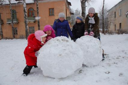 Дети лепят большой ком снега для снеговика.