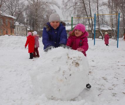 Дети лепят большой ком снега для снеговика.