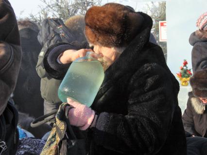 Женщина пьет освященную воду из трехлитровой банки зимой на улице.