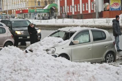 Снежная лавина обрушилась с крыши дома на тротуар и припаркованные автомобили в Барнауле. На снимке: люди у засыпанных снегом поврежденных автомобилей.