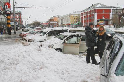 Снежная лавина обрушилась с крыши дома на тротуар и припаркованные автомобили в Барнауле. На снимке: люди стоят у поврежденных автомобилей засыпанных снегом.