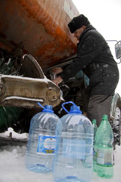 Аварийное отключение воды. На снимке: мужчина наполняет бутылки водой из поливочной машины.