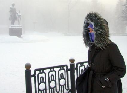 Девушка укутавшись в теплую зимнюю одежду идет по заснеженной улице Барнаула.