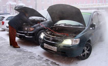 Водитель заводит автомобиль с помощью проводов `прикуривая` от другого автомобиля.