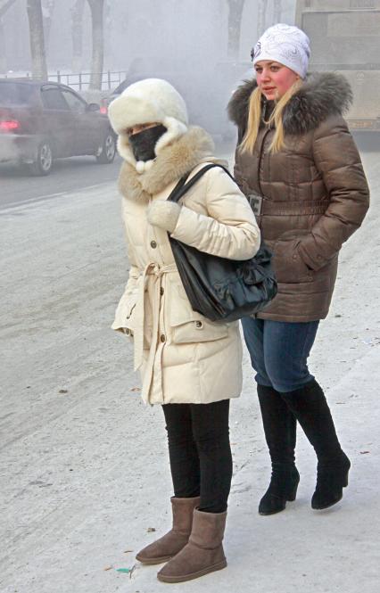 Девушки ожидают общественный транспорт на остановке морозным днем в Барнауле.