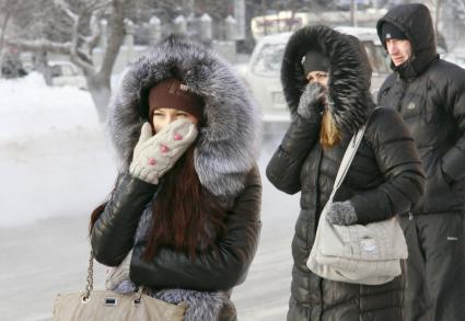 Люди на остановке общественного транспорта закрывают лицо руками от мороза.