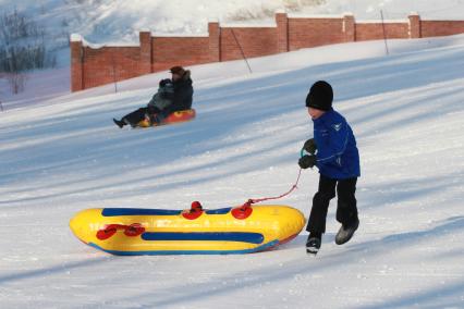 Ребенок бежит по снежной горки и тащит за собой надувную ледянку.