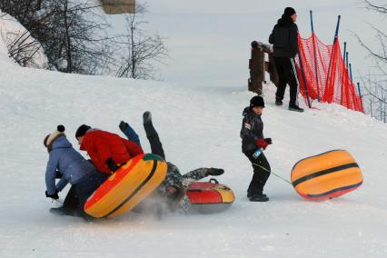 Люди падают с надувных ледянок во время спуска со снежной горки.