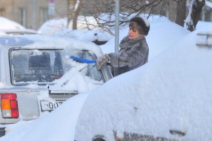 Последствия снегопада. На снимке: женщина чистит автомобиль от снега.