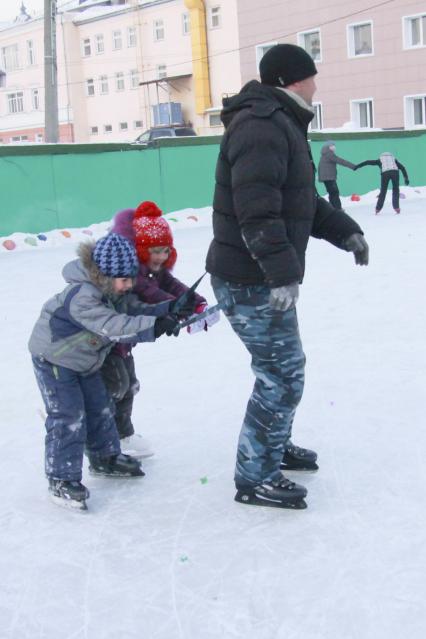 Мужчина катается на коньках сзади за него держатся два ребенка.