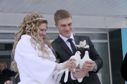 Молодожены зимой на улице держат в руках белых голубей.