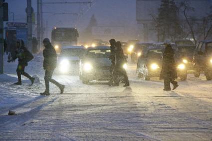 Пешеходы переходят дорогу на перекрестке во время сильного снегопада.