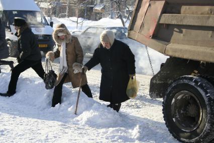 Пешеходы переходя улицу преодолевают большие снежные сугробы.