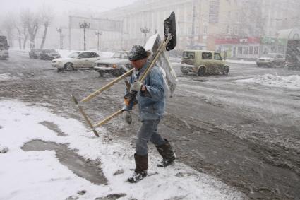Дворник с лопатами переходит улицу во время сильного снегопада.