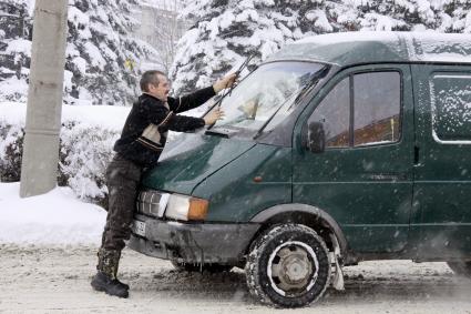 Водитель автомобиля `Газель` чистит дворники во время сильного снегопада.