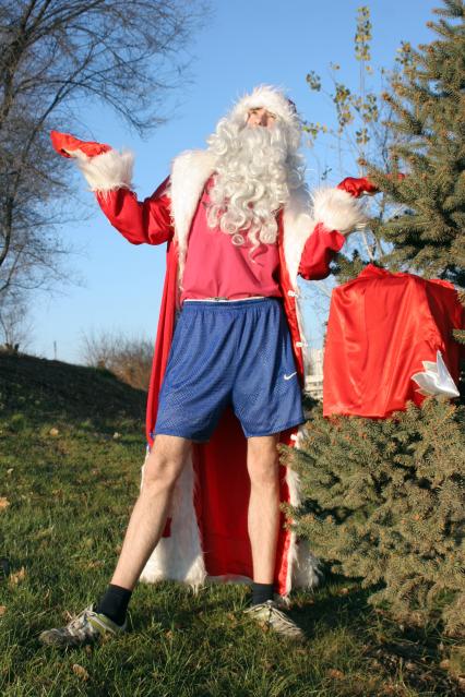 Мужчина переодетый в Деда Мороза в шортах летом ждет зиму.