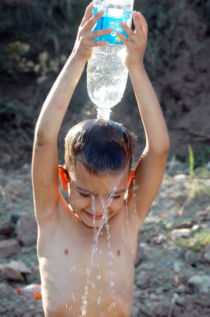 Ребенок поливает себя водой из бутылки.