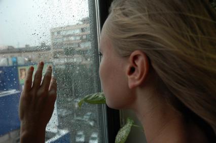 Девушка смотрит в окно, за окном идет дождь.