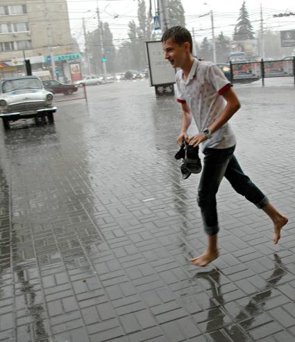 Мужчина босиком бежит по улице под проливным дождем.