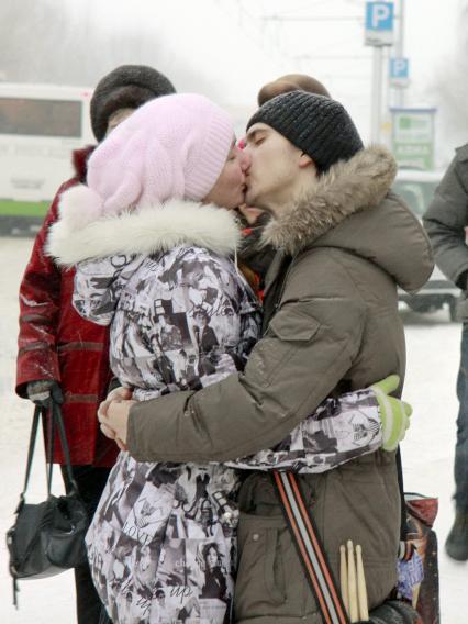 Молодая пара целуется зимой на автобусной остановке.
