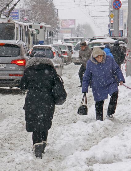 Пешеходы пробираются по заснеженной улице во время сильного снегопада.