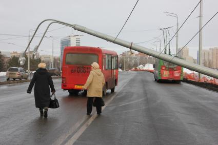 Упал столб освещения, мимо едет автобус и идут две женщины.