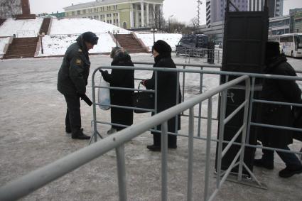 Проход на массовое мероприятие. Полицейский проверяет сумки у людей после прохода через рамку металлоискателя.