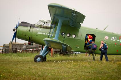 Парашютисты садятся в самолет АН-2 принадлежащий `ДОСААФ России` на поле летом.