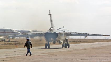 Военный идет по летному полю на фоне работающих двигателя военного самолета фронтового бомбардировщика СУ-24М.