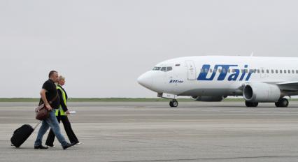 Пассажирский самолет Boeing 737-500 авиакомпания `UTair`. Пассажиры с чемоданами идут по взлетной полосе.