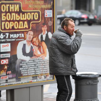 Бомж пьет кофе на улице рядом с урной.