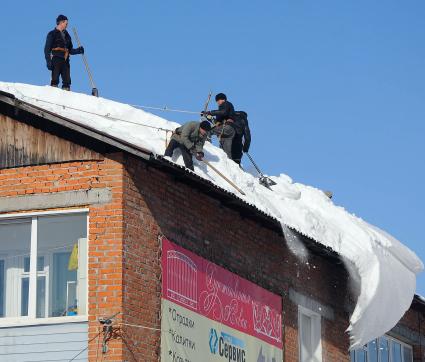 Рабочие отчищают крышу дома от снега.